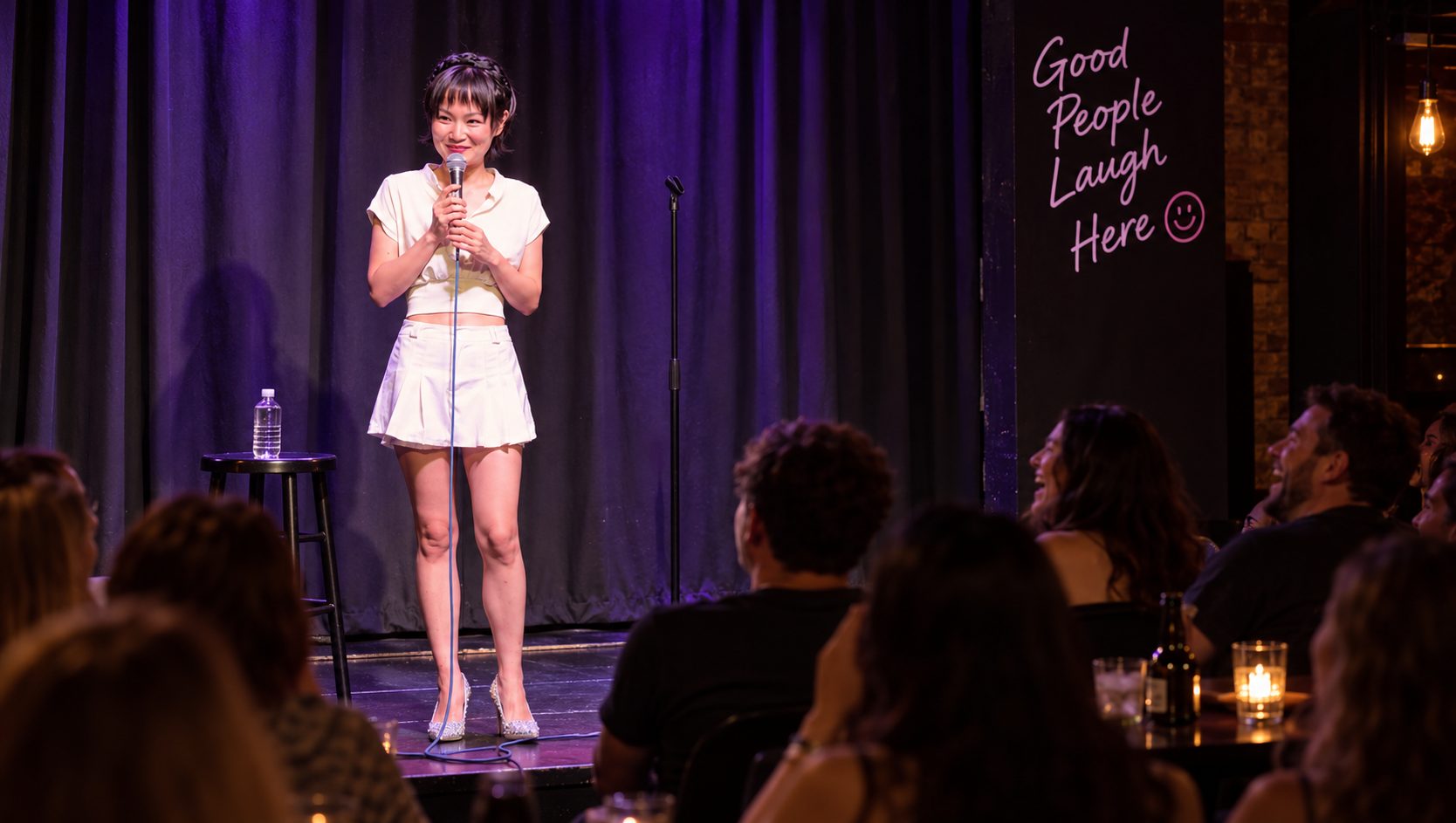 Ginger Phoenix performing stand-up in a white dress in front of a live audience